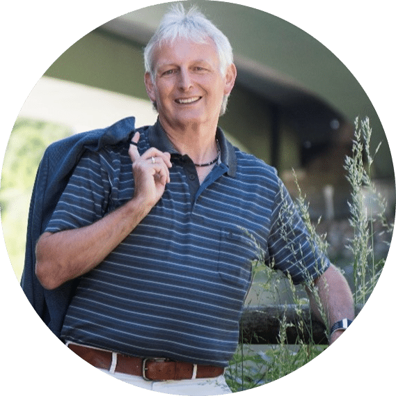 Porträt eines freundlich lächelnden Mannes, Klaus Lichtenauer, mit grauen Haaren, der eine Jacke locker über die Schulter gelegt hat und im Freien steht.